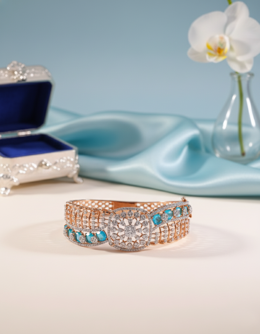 Rose gold bangle with blue stones on a white surface with a blue satin cloth and white orchid in the background.