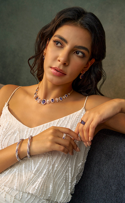 Woman wearing a necklace, ring, and bracelet against a neutral background